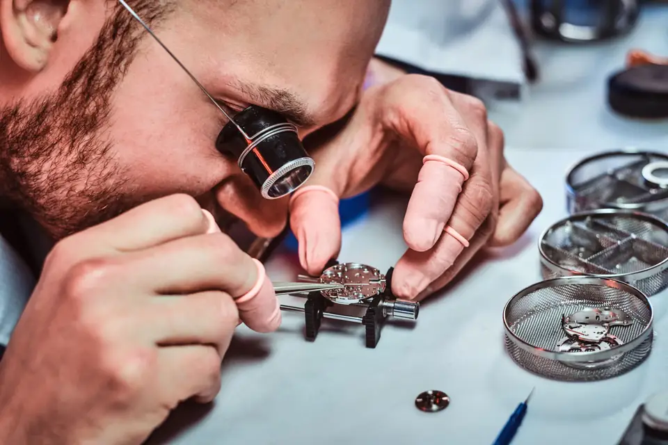 Watchmaker using a loupe and tweezers to work on a watch movement